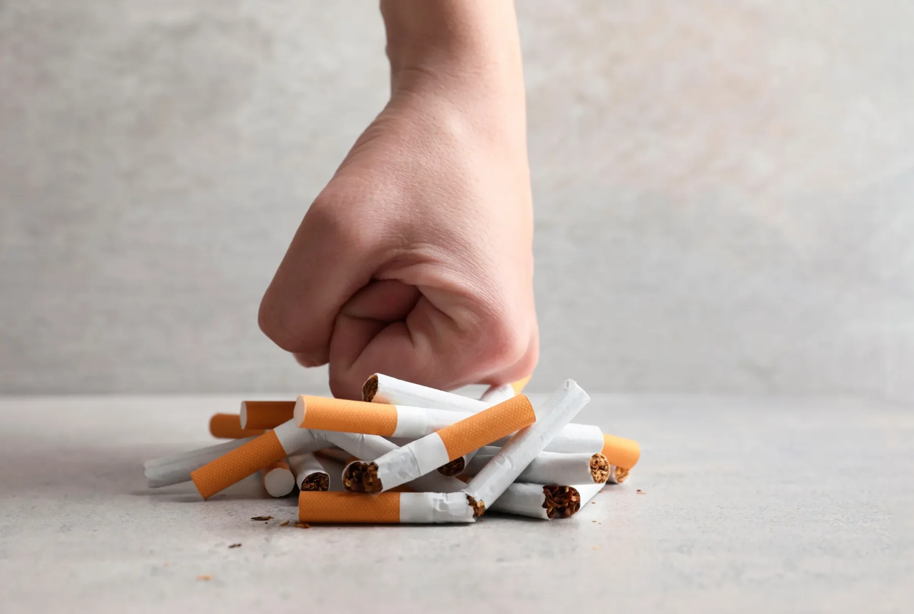 A hand closing over a pile of cigarettes on a plain surface, representing a decision point in a habitual pattern